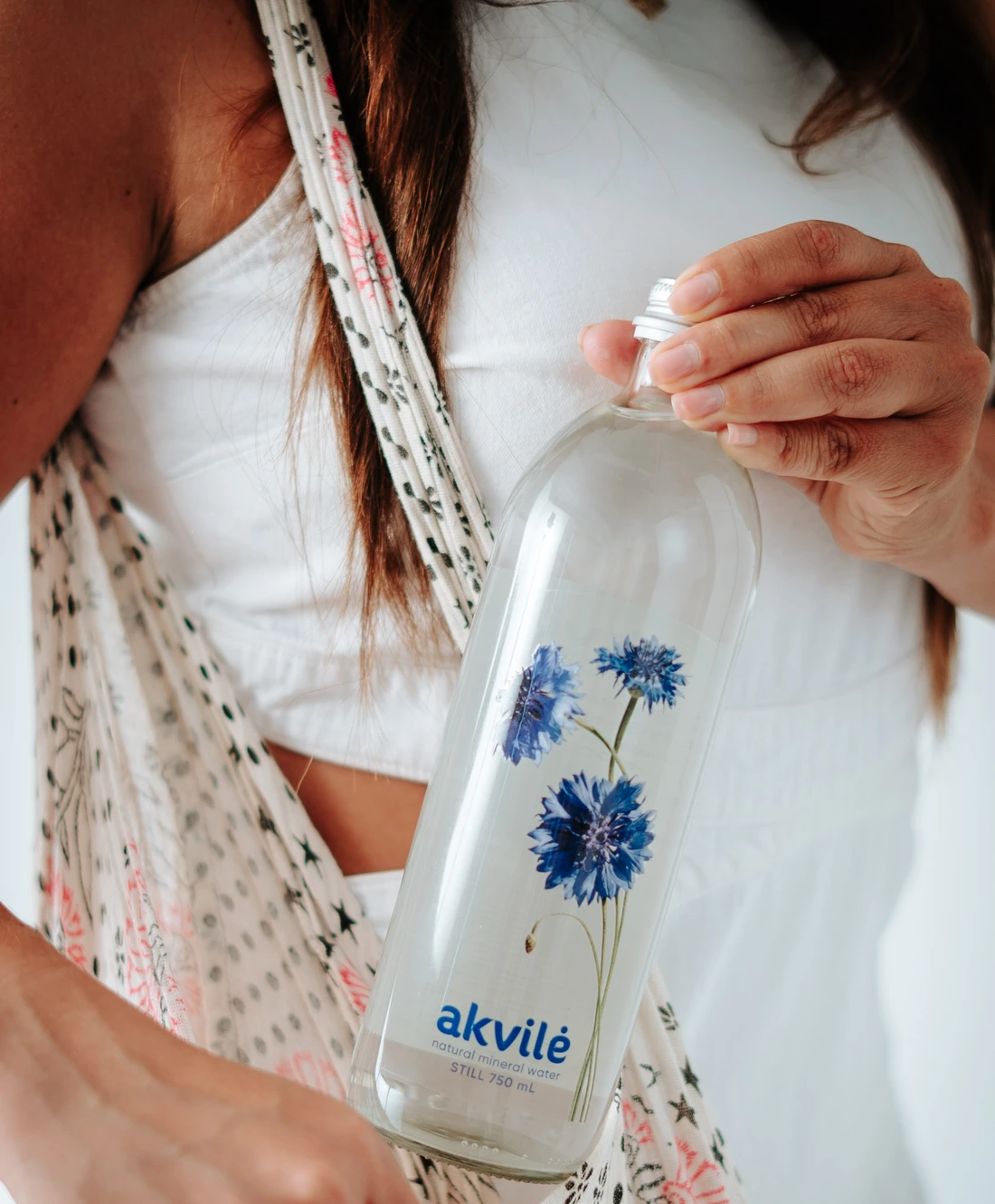 A woman opening an akvilė still 750 mL glass bottle with blue cornflower artwork