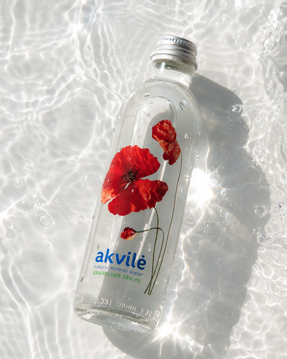 akvilė sparkling natural mineral water 330 mL bottle with red poppy artwork resting in clear sunlit water