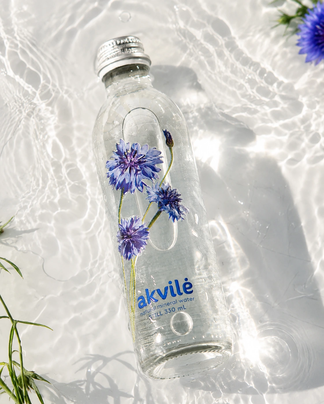 akvilė still natural mineral water 330 mL bottle with blue cornflower artwork resting in clear sunlit water